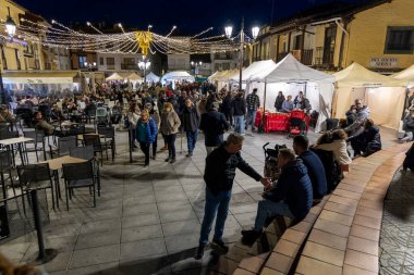 Candeleda, Avila, İspanya, 10 Aralık 2025: Banklarda oturan ve ayakta duran insanlarla dolu bir açık hava pazarı. Atmosfer canlı ve hareketli..