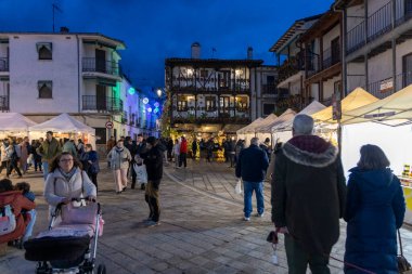 Candeleda, Avila, İspanya, 10 Aralık 2025: Geceleri kalabalık bir cadde, insanların yürüdüğü ve bebek arabasını iten bir kadın. Atmosfer canlı ve hareketli..