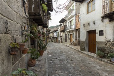 Cuevas del Valle, Avila, Spain, December 10, 2025: A narrow street with a cobblestone road and a row of houses. The houses are old and have a rustic charm.