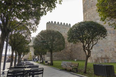 Avila, İspanya, 10 Aralık 2025: Taş duvarı ve birkaç ağacı olan bir avlu. İnsanların oturup yemek yemesi için birkaç bank ve masa var..