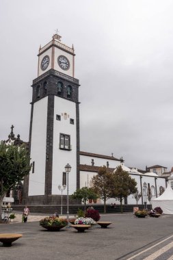 Ponta Delgada, Portekiz, 8 Ekim 2025: Beyaz tabanlı ve siyah kapaklı büyük bir saat kulesi. Saat kulede ve kule de kilisenin önünde. Gökyüzü bulutlu..