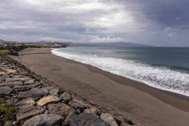 Azores, Portekiz, 8 Ekim 2025, kayalık bir sahil ve bulutlu bir gökyüzü. Kumsal boş ve su sakin.