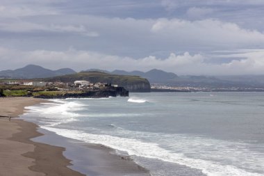 Arka planda büyük bir su kütlesi olan bir plaj. Gökyüzü bulutlu ve kumsal boş.