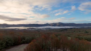 Gökyüzü bulutlu ve arka planda dağlar var. Ağaçlar kahverengidir ve kar Orense, İspanya 'da yerdedir..