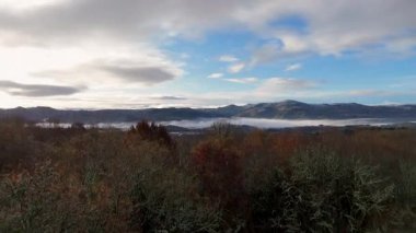 Bulutlu bir gökyüzü ile sisli bir dağın tepesinde uçan bir dron. Gökyüzü mavi ve dağlar Orense, İspanya 'da ağaçlarla kaplı..