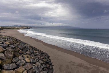 Azores, Portekiz, 8 Ekim 2025: Arkasında büyük bir su kütlesi olan kayalık bir plaj. Gökyüzü bulutlu ve kumsal boş.