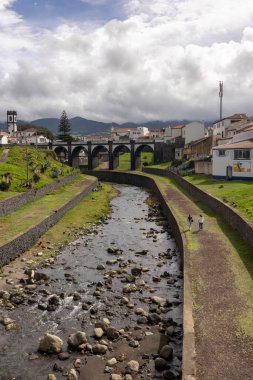 Ribeira Grande, Azores, Portekiz, 8 Ekim 2025: Köprüsü ve arka planda bir kasabası olan bir nehir. Köprü eski ve kasaba küçük.