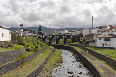 Ribeira Grande, Azores, Portekiz, 8 Ekim 2025, içinden bir nehir akan küçük bir kasaba. Nehir taştan bir duvarla çevrili ve evler beyaz.