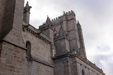 Çan kulesi ve saat kulesi olan büyük bir taş bina. Bina eski ve Gotik bir tarzı var. Gökyüzü bulutlu ve bina bir avluyla çevrili.