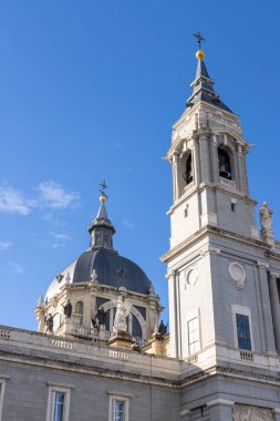 Ayırt edici çan kulesi ve açık mavi gökyüzüne karşı kubbesi ile Almudena katedrali cephesi
