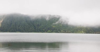 Furnas lagününün arka planında bir gölle sisli bir gün, Azores. Su sakin ve gökyüzü kapalı.