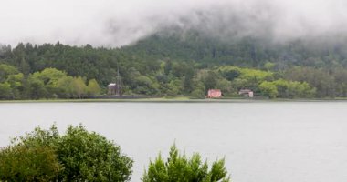 Furnas lagününün arka planında bir gölle sisli bir gün, Azores. Su sakin ve gökyüzü kapalı.