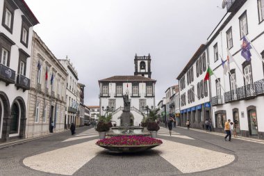 Ponta Delgada, Portekiz, 8 Ekim 2025: Merkezi fıskiye ve heykel olan bir şehir meydanı. İnsanlar etrafta dolanıyor ve binalardan bayraklar sarkıyor.