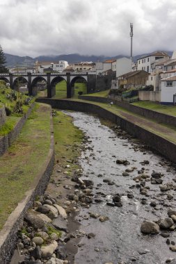 Ribeira Grande, Azores, Portekiz, 8 Ekim 2025: Her iki tarafında evleri olan bir nehir akar. Su bulanık ve nehir yatağındaki kayalar büyük.
