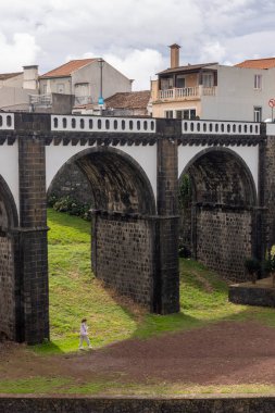 Ribeira Grande, Azores, Portekiz, 8 Ekim 2025: Bir kadın nehir üzerinde bir köprüde yürüyor. Köprü eski ve taş bir kemeri var.