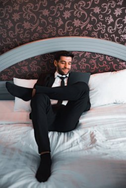 Handsome young bearded businessman lying on bed with tablet