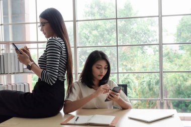 İki Asyalı iş kadını cep telefonu kullanıyor.