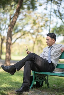 İş adamı bankta oturuyor ve cep telefonu kullanıyor