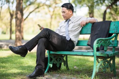 İş adamı bankta oturuyor ve cep telefonu kullanıyor