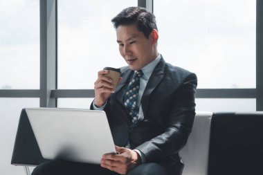 Asyalı iş adamı laptopla çalışıyor ve kahve içiyor.