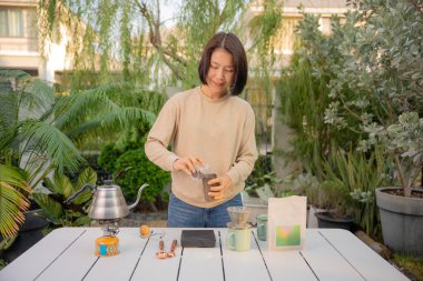 Asyalı bir kadın evinin bahçesinde kahve çekirdeği damlatıyor..