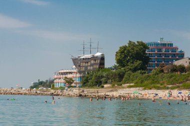 Tahta yelkenli gemi - Sirius restoranı ve Sirius oteli ve deniz sahillerindeki insanlar, St. Constantine ve Helena tatil beldesi, Varna ili, Bulgaristan.