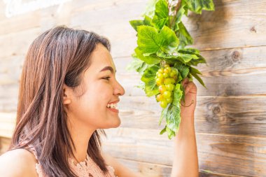 Tahta arka planda olgun üzümleri tutan güzel bir genç kadının portresi.