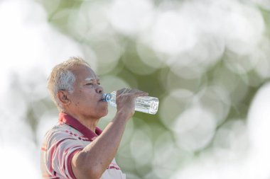 Asyalı yaşlı bir adamın portresi. Şişeden su içen olgun bir adam. Soyut, güzel, yeşil bir arka plan.