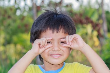 Bahçedeki kameraya göz teması kurarak gülümseyen Asyalı çocuğun açık hava portresi.