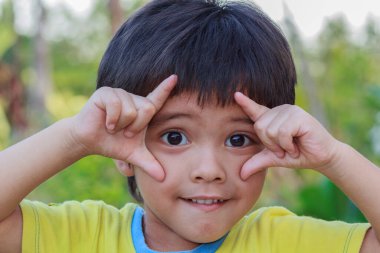 Asyalı küçük bir çocuğun kamera ile göz teması kurarak gülümseyen yüzünün açık hava portresi.
