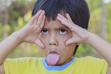 Mutlu Asyalı şirin Taylandlı çocuğun portresi parmaklarıyla gözlerini yuvarlıyor ve dilini dışarı çıkarıyor.