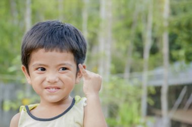 Gülümseyen Asyalı küçük sevimli çocuğa serçe parmağı göster ya da jest konseptini uzlaştır ve yeşil arka plandaki kameraya bak.