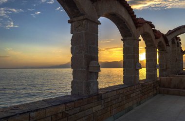 Gün batımı ve deniz manzarası taş kemerlerden yapılmış bir duvarın ardında..