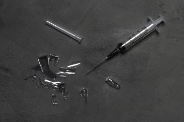 Kullanılan tek kullanımlık şırınga ve gri beton arka plandaki enjeksiyon ampulünden parçalar..