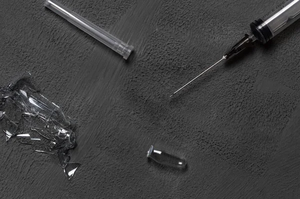 A used disposable syringe and fragments from an injection ampoule on a gray concrete background.