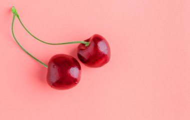 Pembe arka planda iki olgun kiraz. Boşluğu kopyala.