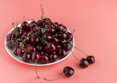 Beyaz bir tabakta olgun, tatlı bir kiraz. Uzayı kopyala Pembe arkaplan.