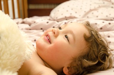 Küçük çocuk yatakta gülümsüyor.