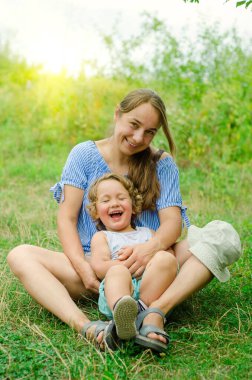 Anne ve çocuk güneşli bir günde çimlerin üzerinde oturuyorlar.
