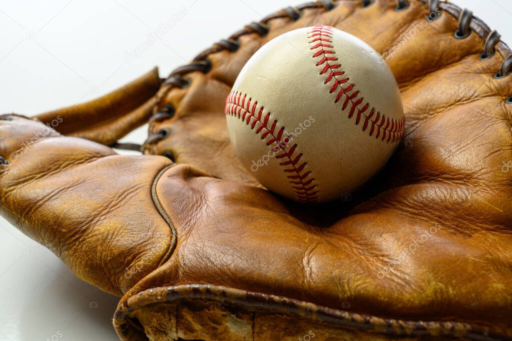 A white leather baseball in a brown vintage, antique glove