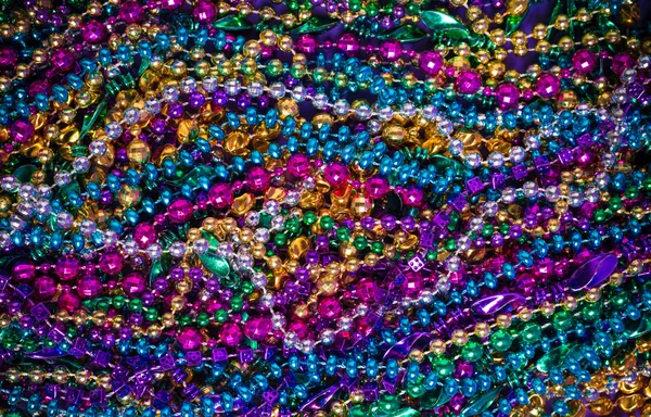 A background of  brightly colored Mardi-Gras beads on a purple b — Stock Photo, Image
