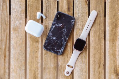 Gelendzhik, Rusya, 29 / 07 / 2020: Kırık arka cam iPhone paneli Apple Watch ve kulaklıkların yanındaki ahşap masada yatıyor