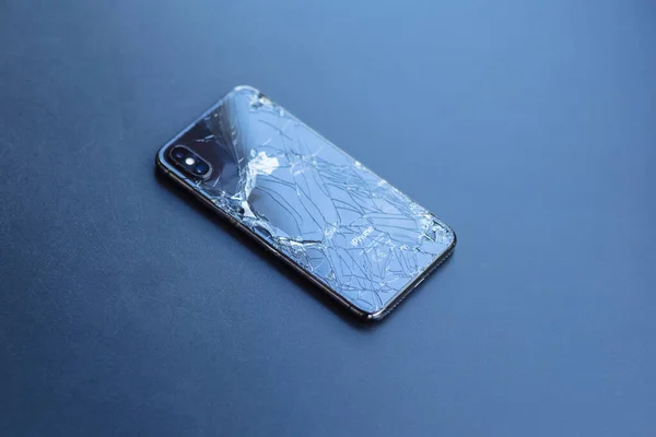 Gelendzhik, Rusya, 07 / 29 / 2020: Kırık sırt kapağı çatlak ve çiplerle kaplı iPhone koyu metal masa yüzeyinde yatıyor