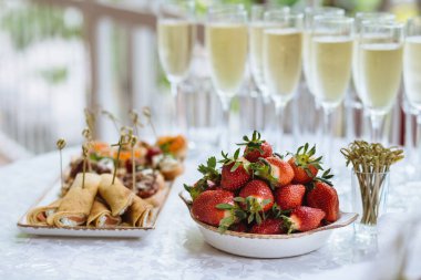 Olgun kırmızı çilek yakın plan büyük miktarlarda aperatif olarak tabakta uzanır arka planda bulanık ve zarif şampanya kadehleri. Büfe masası, tatil partisi, yetişkin masası, piknik..