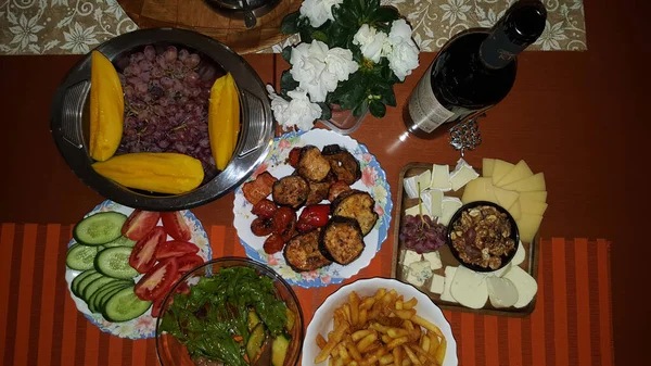 Prato de queijo uvas e manga legumes grelhados pepinos e tomates e uma garrafa de vinho — Fotografia de Stock