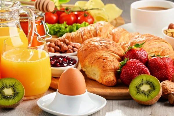 Breakfast consisting of croissants, coffee, fruits, orange juice
