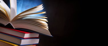 Bir yığın kitabın üzerinde açık bir kitap bulunan kompozisyon. 