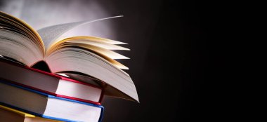 Bir yığın kitabın üzerinde açık bir kitap bulunan kompozisyon. 