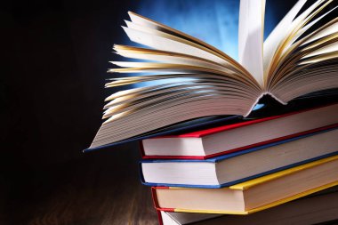 Bir yığın kitabın üzerinde açık bir kitap bulunan kompozisyon. 