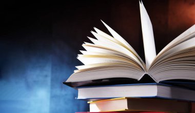 Bir yığın kitabın üzerinde açık bir kitap bulunan kompozisyon. 